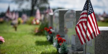 Cemetery with grave markers, flowers, and American flags.
