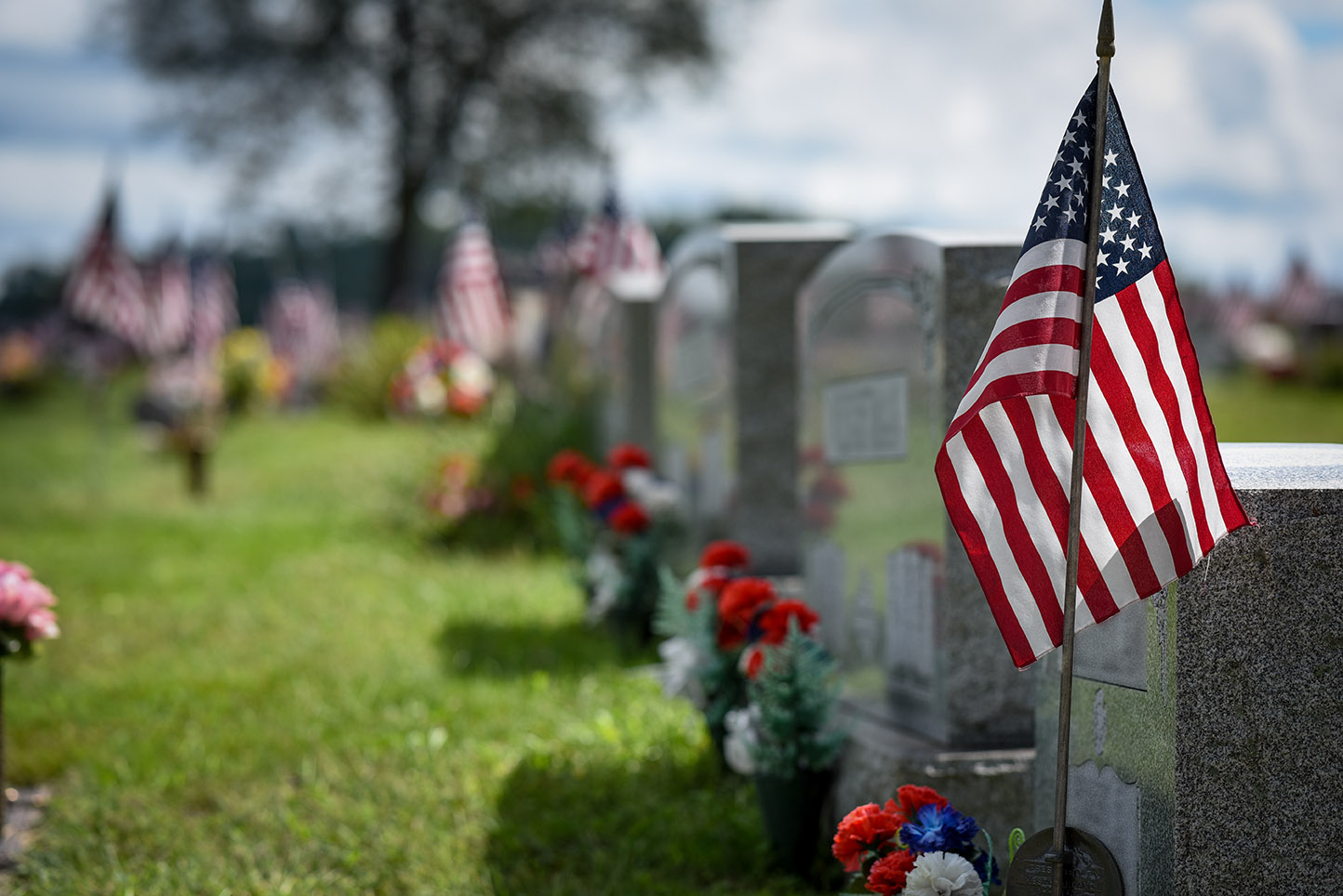 Cemetery with grave markers, flowers, and American flags.